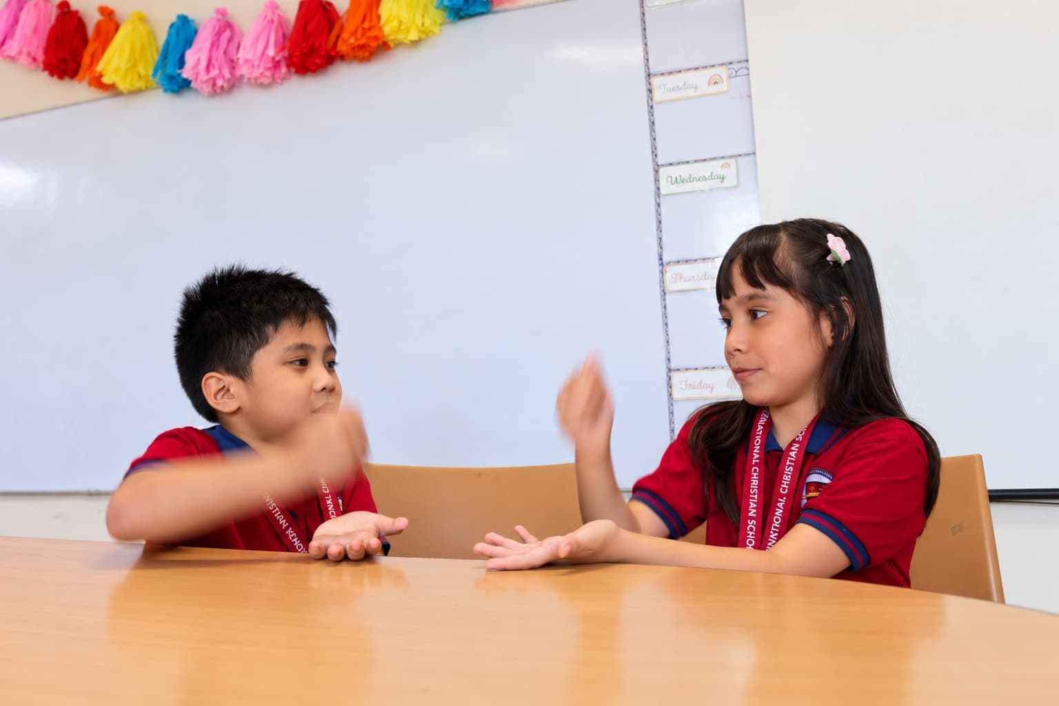 Two young students at Leaders learning together through a hand game.