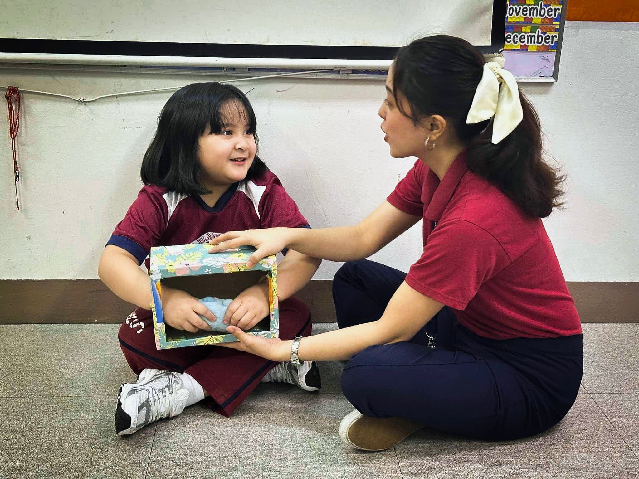 A teacher sitting beside a young student as they share a book at Leaders.